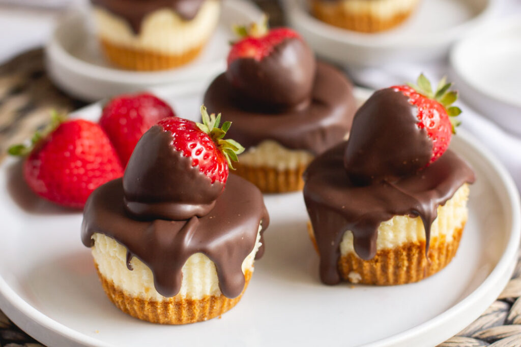 mini cheesecakes on a plate with chocolate covered strawberries on top and chocolate dripping down