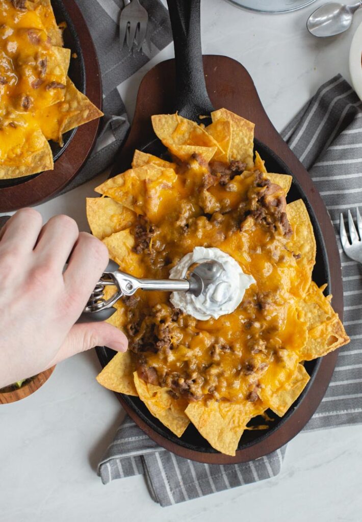 restaurant style beef nachos being topped with sour cream