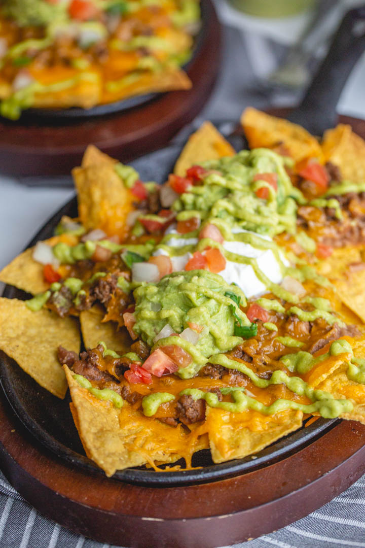 restaurant style beef nachos in a cast iron skillet topped with cheese, tomatoes, guacamole and more
