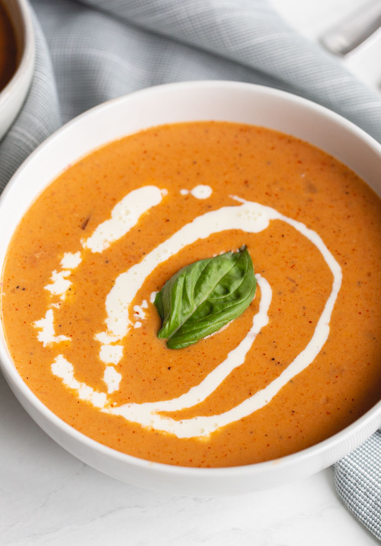 Roasted Red Pepper and Tomato Soup garnished with a basil leaf and swirl of cream