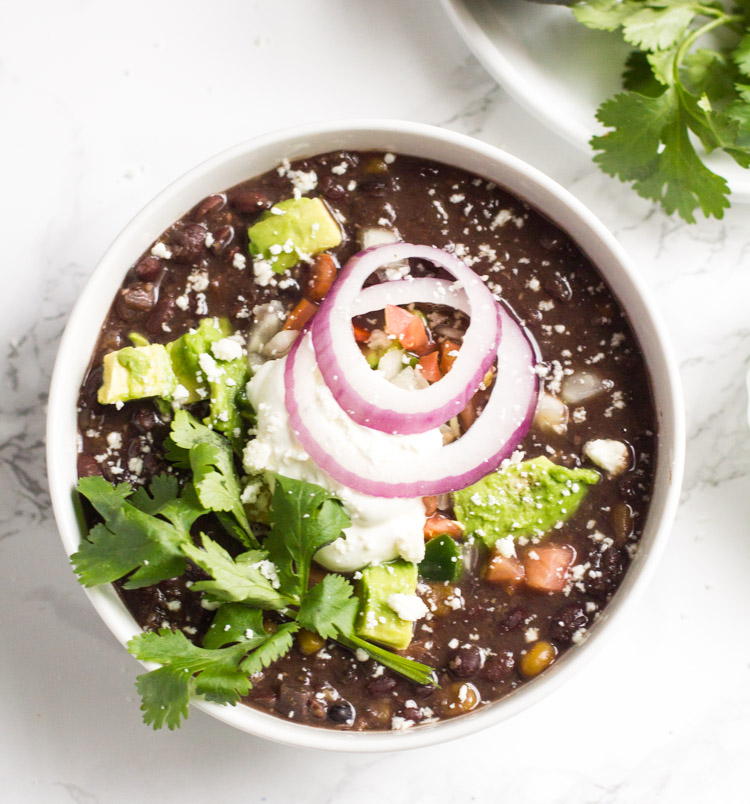 black bean soup in a bowl with cilantro, onions and sour cream on top