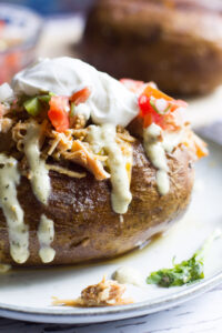 These easy baked potatoes are topped with a slow cooked Tex Mex style pulled pork, cheese, pico de gallo and jalapeno ranch. A hearty and easy to prepare meal!