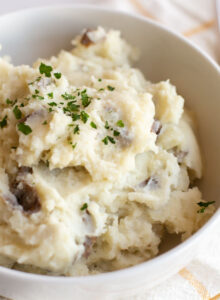 A closeup of mashed potatoes in a white bowl with some parsley on top