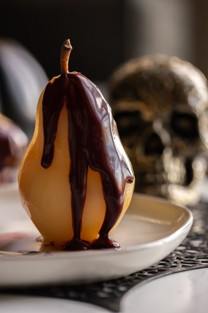 Easy poached pears sitting on a dish with red velvet sauce on top.