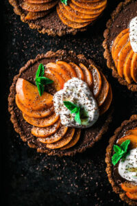 dark chocolate tarts filled with ganache and topped with apricots and cream against a black backdrop