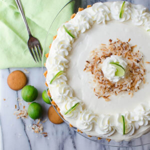 key lime mousse tart topped with whipped cream, lime and coconut, with limes and nilla wafers in the background