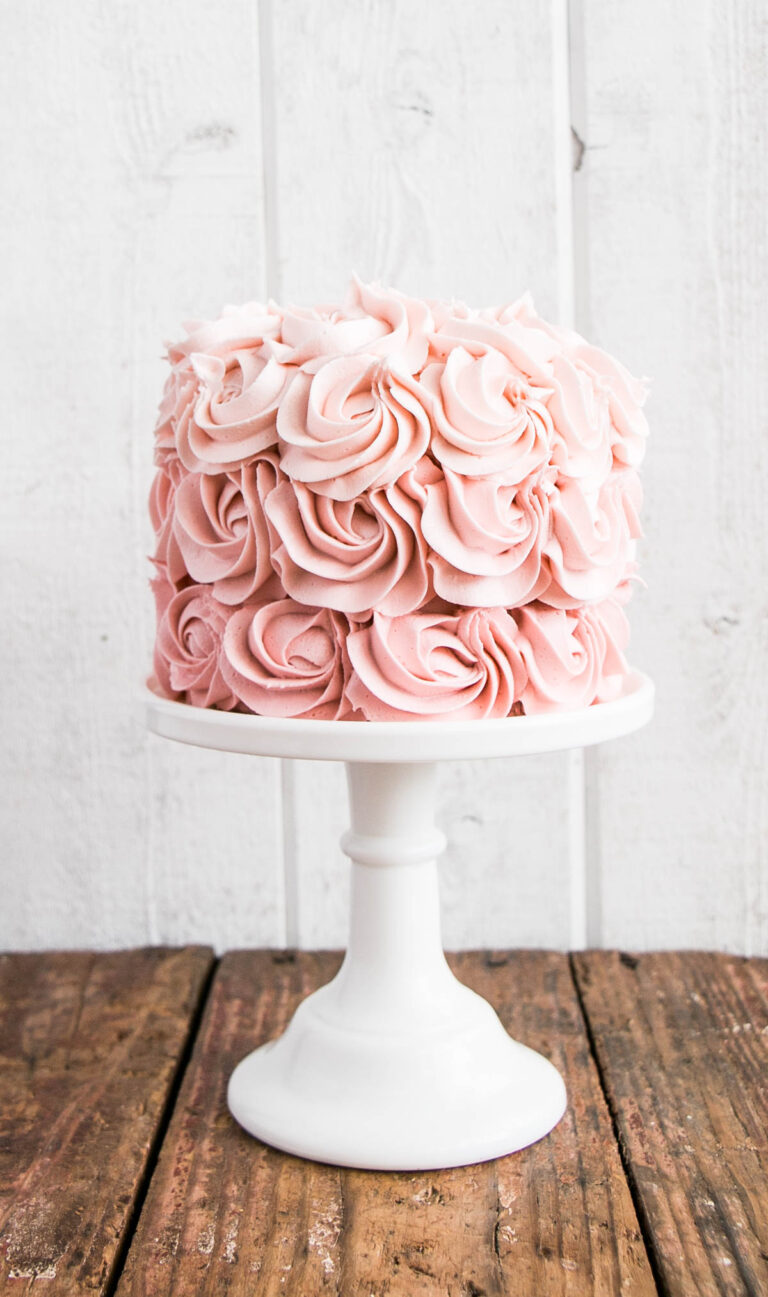 a pink ombre rosette cake on a white cake stand against a white backdrop