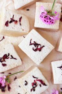 hibiscus rose hip marshmallows dusted with powdered sugar and topped with flowers against a beige background