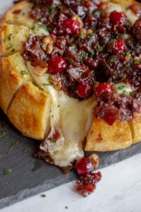baked brie with cranberries and bacon on a plate with brie oozing out