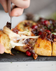 baked brie with cranberries and bacon being pulled apart with stretchy cheese