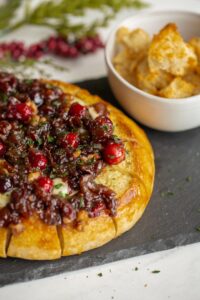 baked brie with cranberries and bacon on a plate with bread crumbs for serving