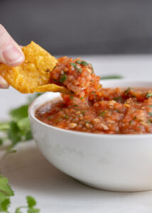 roasted red salsa in a bowl with a chip scooping some out to eat