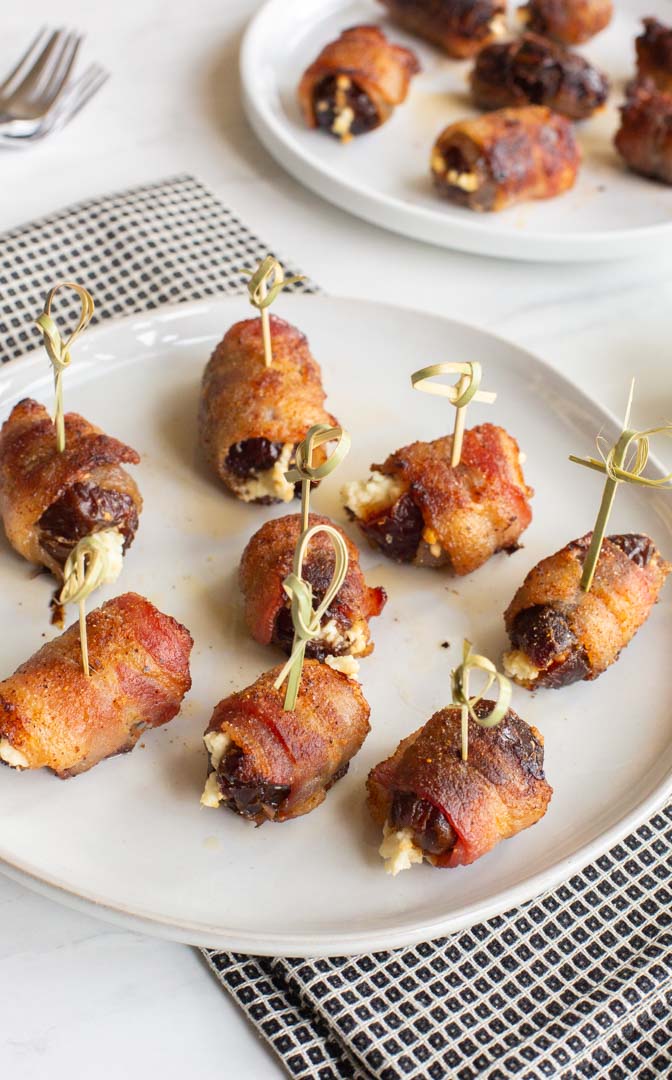 bacon wrapped dates with goat cheese on a plate with skewers