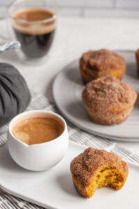 several pumpkin muffins on a plate with coffee and cinnamon sugar