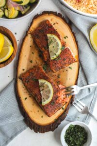 two filets of blackened salmon on a cedar plank with lemon slices