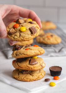 hand placing peanut butter cup cookie on top of large stack of cookies