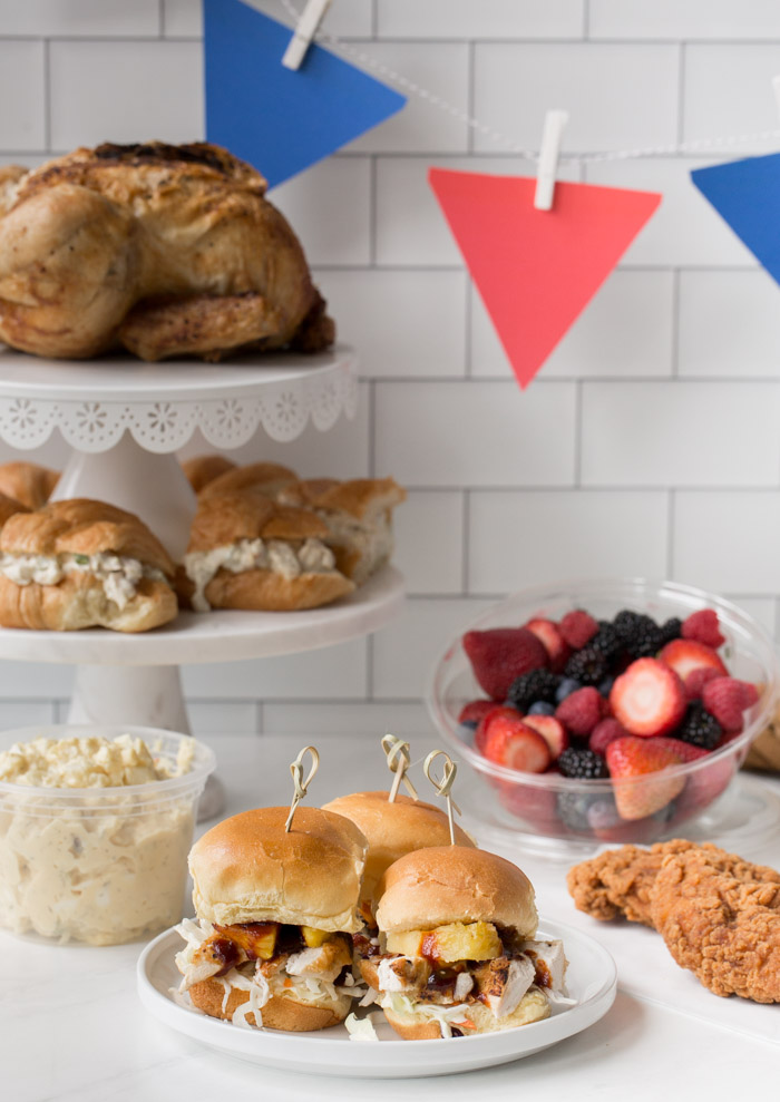 bbq sliders, fresh fruit, cookies, sandwiches and chicken laid out in a party spread