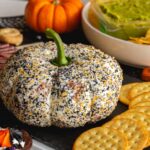 a pumpkin shaped cheese ball covered in everything bagel seasoning and served with crackers