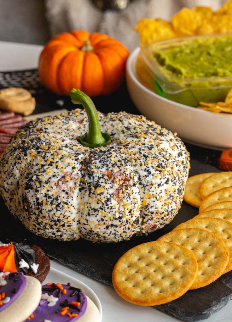 a pumpkin shaped cheese ball covered in everything bagel seasoning and served with crackers