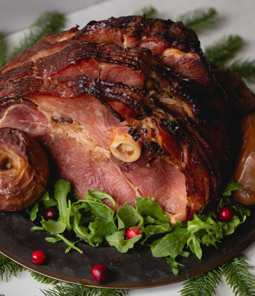 a glazed holiday ham served with baked apples, arugula and cranberries