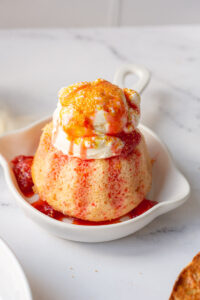 mini bundt cake topped with vanilla ice cream, strawberry sauce and gold sprinkles