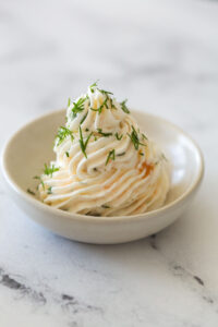 salmon mousse piped onto a white dish topped with fresh dill against a white marble background